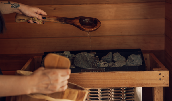 hand pouring water on stones in a sauna